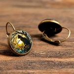 Pair of earrings with wolf and moon design on a wooden surface