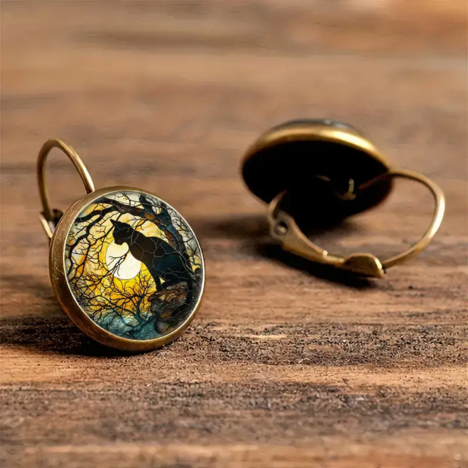 Pair of earrings with wolf and moon design on a wooden surface