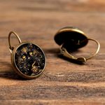 Pair of bronze earrings with intricate designs on a wooden surface