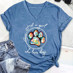 Blue t-shirt with colorful paw print and text 'just a girl who loves dogs' on a white surface with jeans and sunglasses.