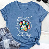 Blue t-shirt with colorful paw print and text 'just a girl who loves dogs' on a white surface with jeans and sunglasses.