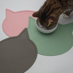 Cat eating from a bowl on a pink, green, and gray cat-shaped mat.