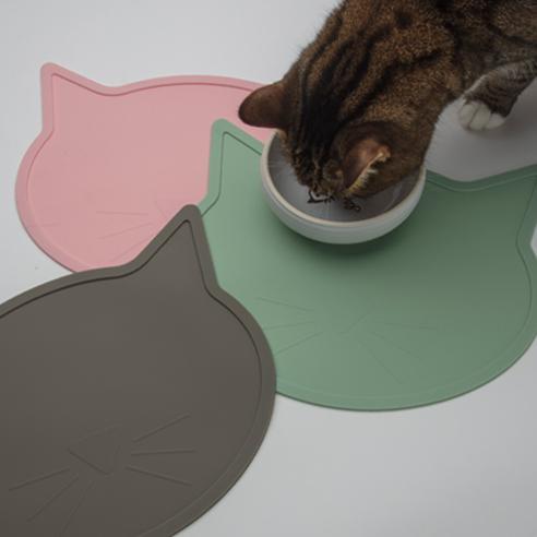 Cat eating from a bowl on a pink, green, and gray cat-shaped mat.