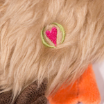 Close-up of a plush toy with a pink heart embroidered on beige fur.