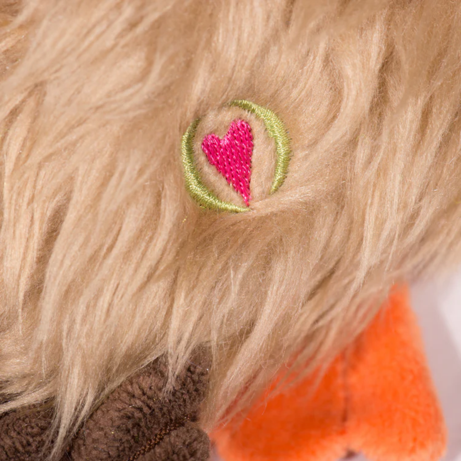 Close-up of a plush toy with a pink heart embroidered on beige fur.