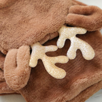 Close-up of a plush brown hooded garment or blanket with glittery gold antler-like accents on a soft brown fabric background.