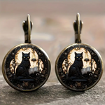 Pair of earrings with black cat design on a blurred background