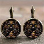 Pair of earrings with intricate designs of a cat and cup on a dark background