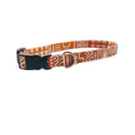 A cat collar with a vibrant orange and white geometric pattern, featuring a black plastic buckle and a silver metal D-ring, displayed on a clean white background.