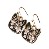 Pair of gold and black floral earrings on a wooden surface