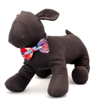 A dark brown plush dog toy wearing a red, white, and blue patterned bow tie, photographed on a clean white background.