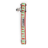 A festive cat collar with a silver bell, featuring a mint green background printed with red and green Christmas trees, red dots, and the text 'WISHING CAT' in black.