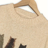 Beige sweater with cat pattern on a wooden hanger against a white background