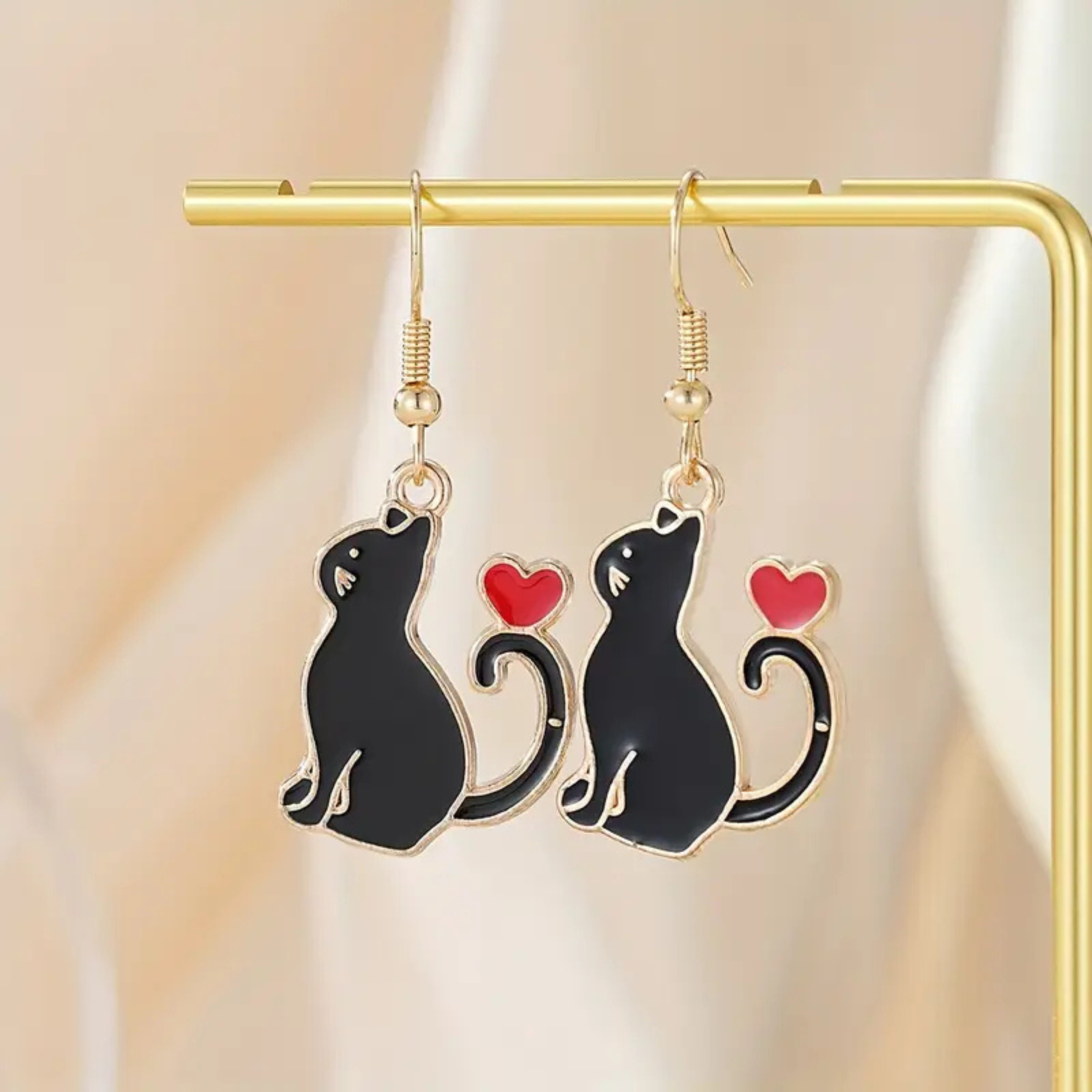 Cat-shaped earrings with red hearts on a gold earring stand against a beige background