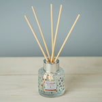 Reed diffuser with wooden sticks in a glass bottle on a wooden surface.