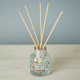 Reed diffuser with wooden sticks in a glass bottle on a wooden surface.