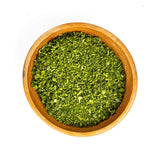Wooden bowl filled with green dried herbs on a white background