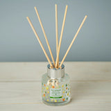 Reed diffuser with wooden sticks in a glass bottle on a wooden surface with a gray background