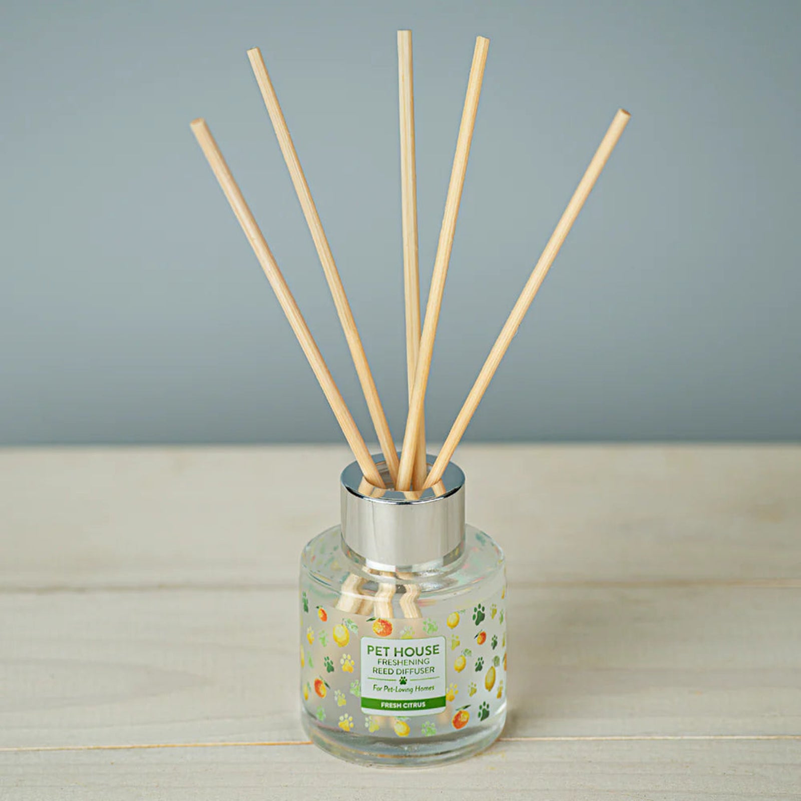 Reed diffuser with wooden sticks in a glass bottle on a wooden surface with a gray background