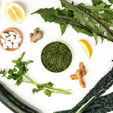 Green smoothie bowl with ingredients including lemon, ginger, turmeric, and greens on a white background