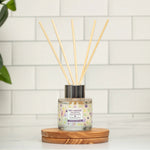 Reed diffuser on a wooden coaster with a clock and plant in the background
