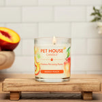 Pet House Candle labeled 'Mango Peach' on a wooden stand with fruits and flowers in the background.