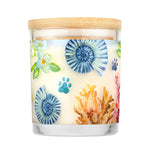 Candle with a decorative label featuring floral and coral designs on a white background