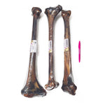 Three rawhide bones with plastic wrap and a pen for scale on a white background