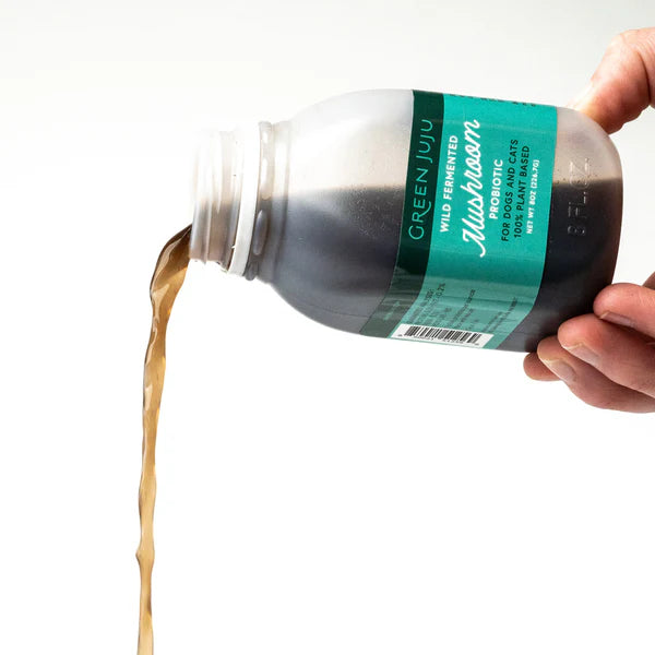 Hand pouring a dark liquid from a bottle labeled 'Green Juju' on a white background