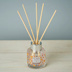 Reed diffuser with wooden sticks in a clear bottle on a wooden surface with a gray background
