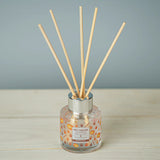 Reed diffuser with wooden sticks in a clear bottle on a wooden surface with a gray background