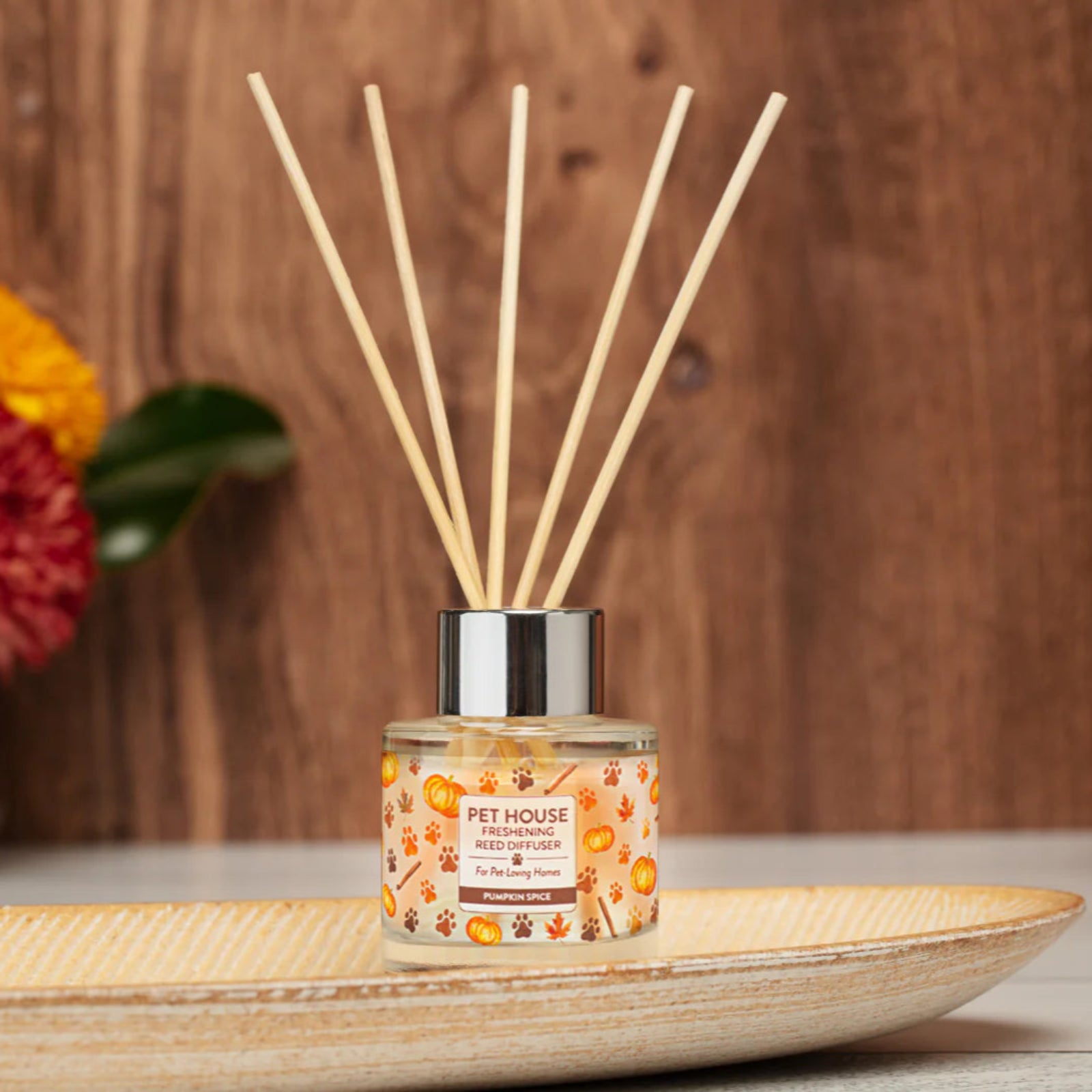 Reed diffuser with floral design on a wooden surface with decorative flowers in the background