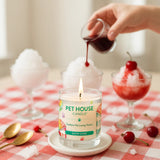 Pet House Candle being lit on a table with a snow cone-themed label, surrounded by cherry treats.