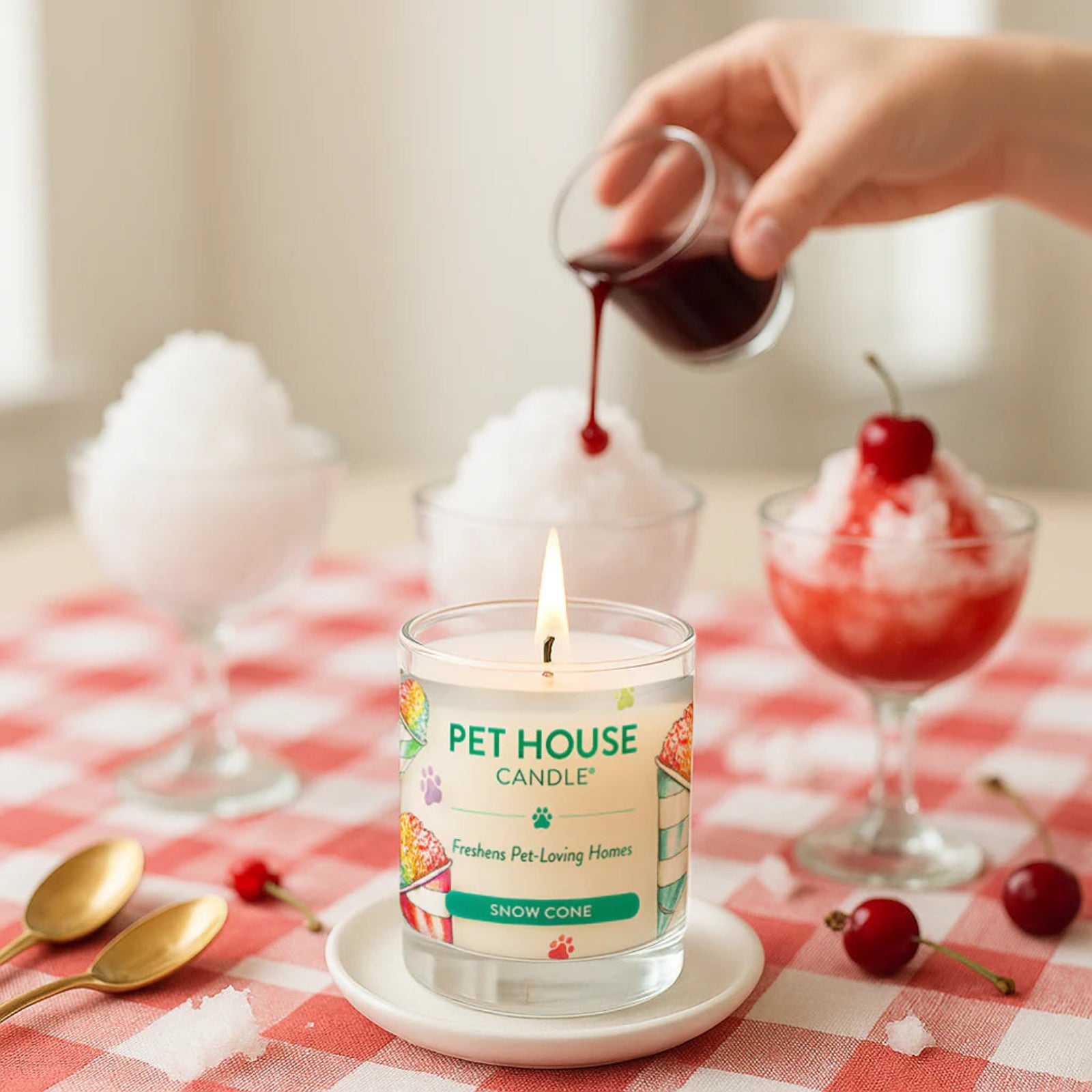 Pet House Candle being lit on a table with a snow cone-themed label, surrounded by cherry treats.