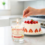 Person lighting a 'Pet House Candle' next to a strawberry shortcake.