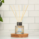 Diffuser with sticks on a wooden coaster against a tiled wall.