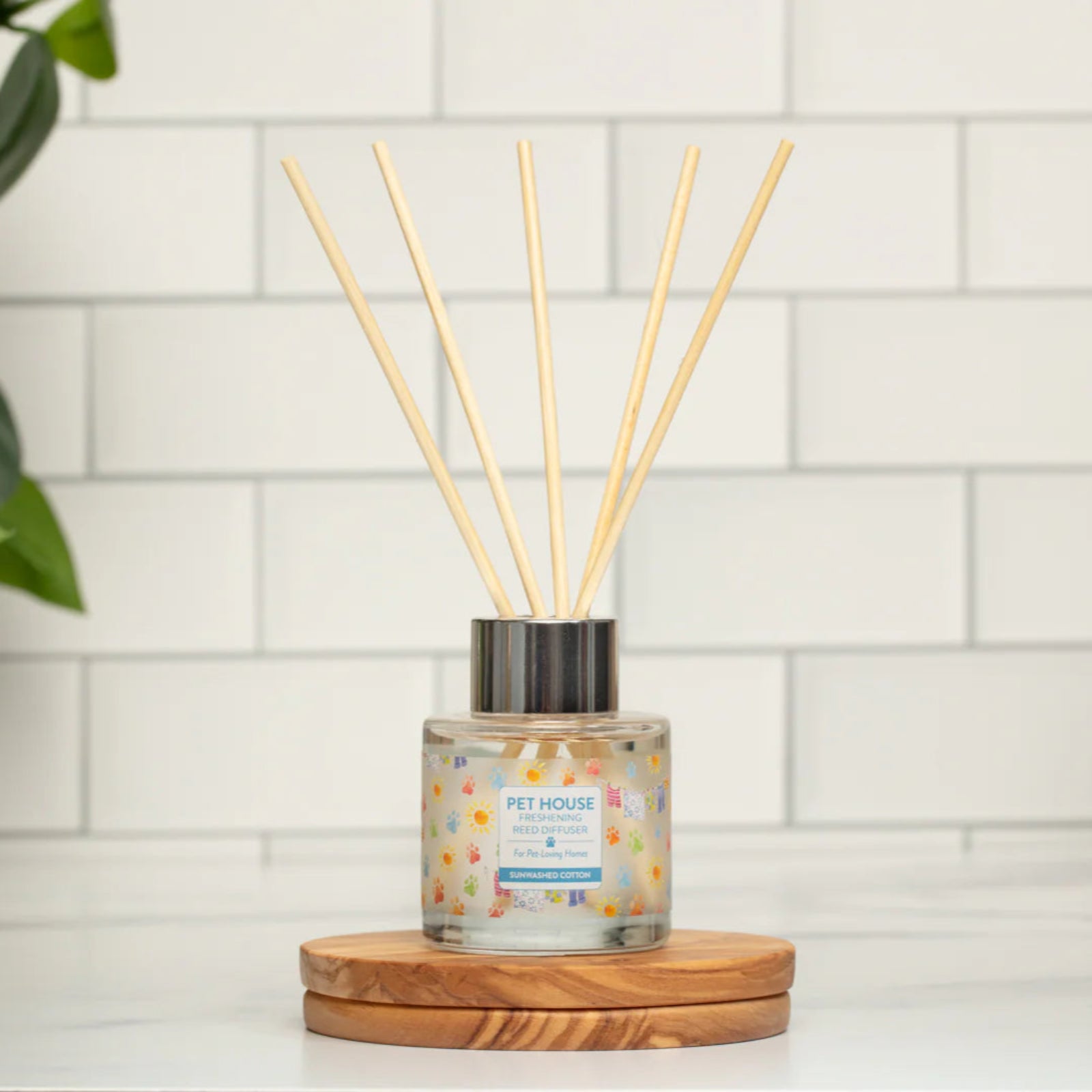 Diffuser with sticks on a wooden coaster against a tiled wall.