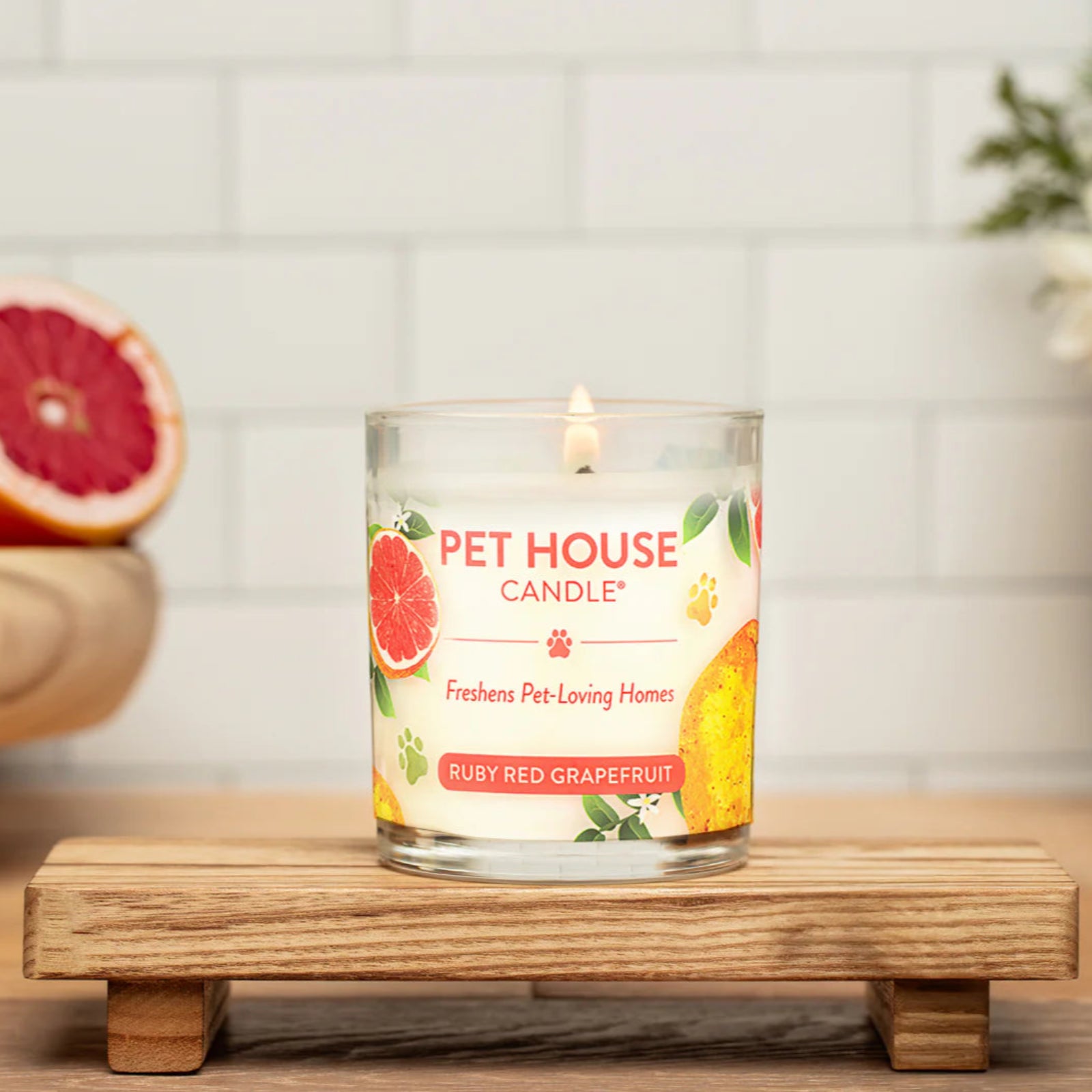 Pet House Candle on a wooden stand with fruits and flowers in the background