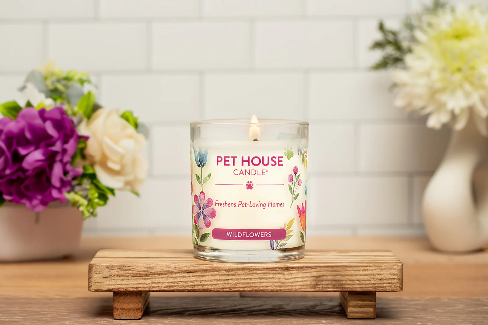 Pet House Candle with floral design on a wooden stand with flowers in the background