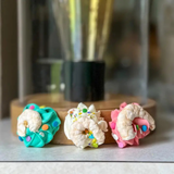 Three colorful donut-shaped cookies on a wooden board with a blurred background.