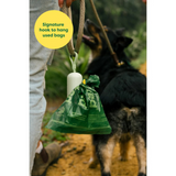 Green dog waste bag holder with a signature hook for hanging bags, featuring a dog in the background.