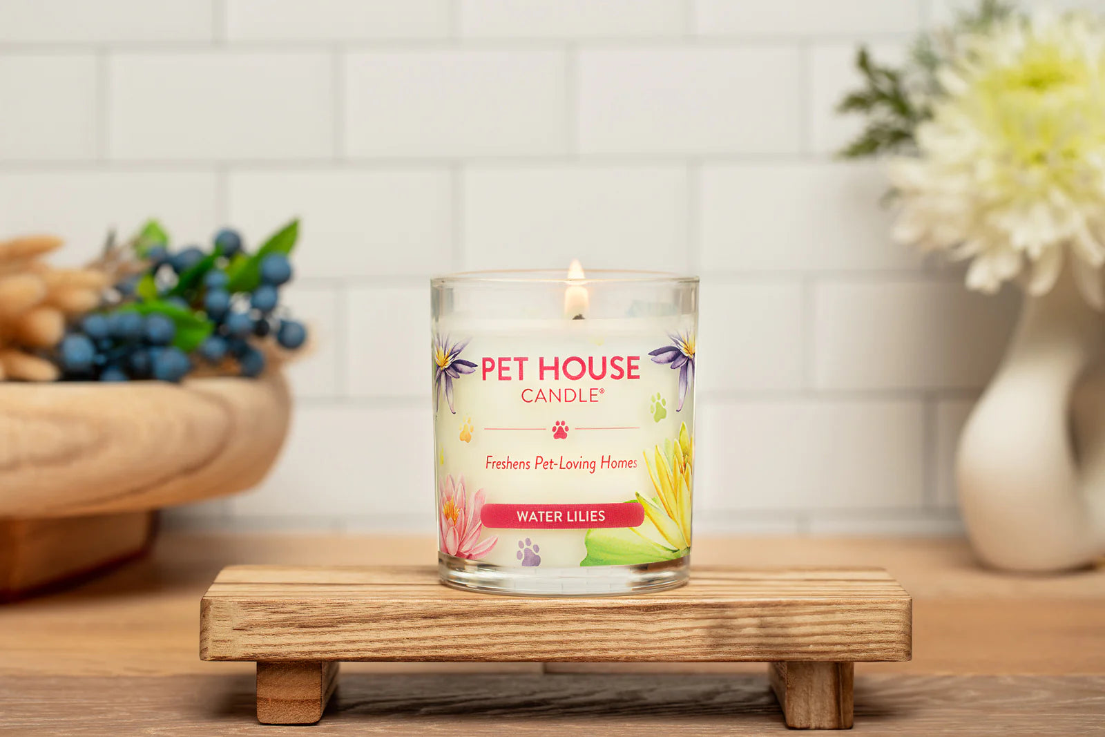 Pet House Candle on a wooden stand with flowers and a bowl in the background