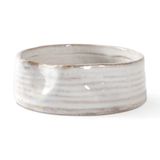 A handmade ceramic bowl with a textured, ribbed exterior and a smooth, glossy off-white interior, shown on a plain white background.