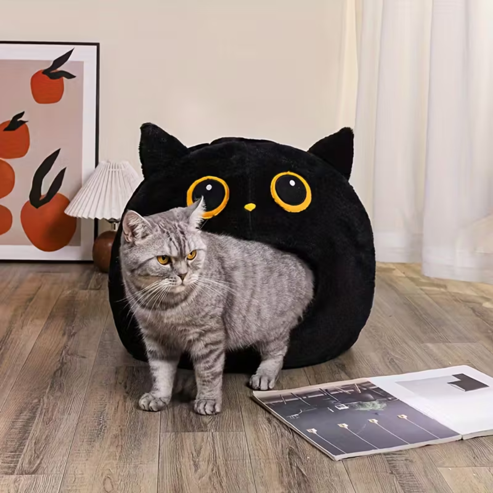 Cat sitting next to a black cat-shaped cushion on a wooden floor.