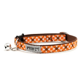 An orange and brown plaid cat collar with a silver metal bell and a central silver brand tag that reads 'WORTHY CAT'.