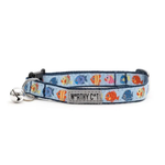 A blue pet collar with a colorful fish pattern, featuring a silver bell and a metal brand tag that reads 'WORTHY CAT'.