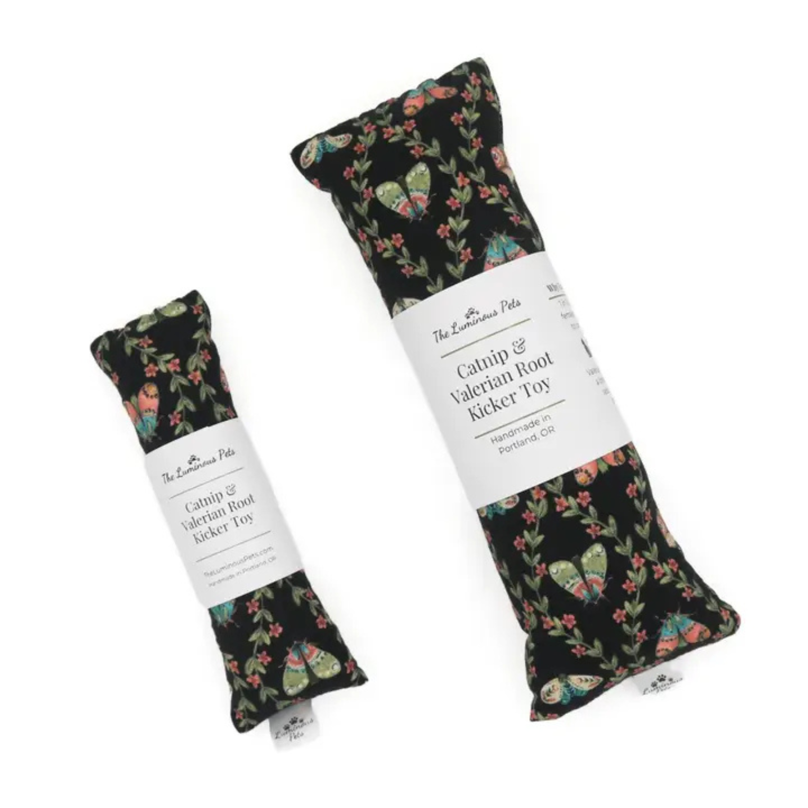 Two fabric-covered foot-shaped toys with white paper labels, shown on a plain white background. The larger toy is upright and the smaller one lies diagonally beside it.