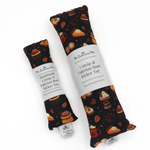 Two fabric catnip root kicker toys by The Luminous Pets, one small and one large, both featuring a dark background with a pattern of cupcakes, coffee cups, and autumn leaves, wrapped in white paper labels.