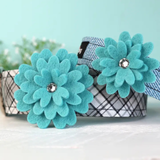 A pet collar with a black, white, and gray plaid pattern, decorated with two large turquoise felt flowers on the front, each with a small clear rhinestone center.