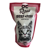 A bag of OC Raw Beef + Fish recipe for cats, featuring a white and pink package with a detailed black and white cat illustration on the front.